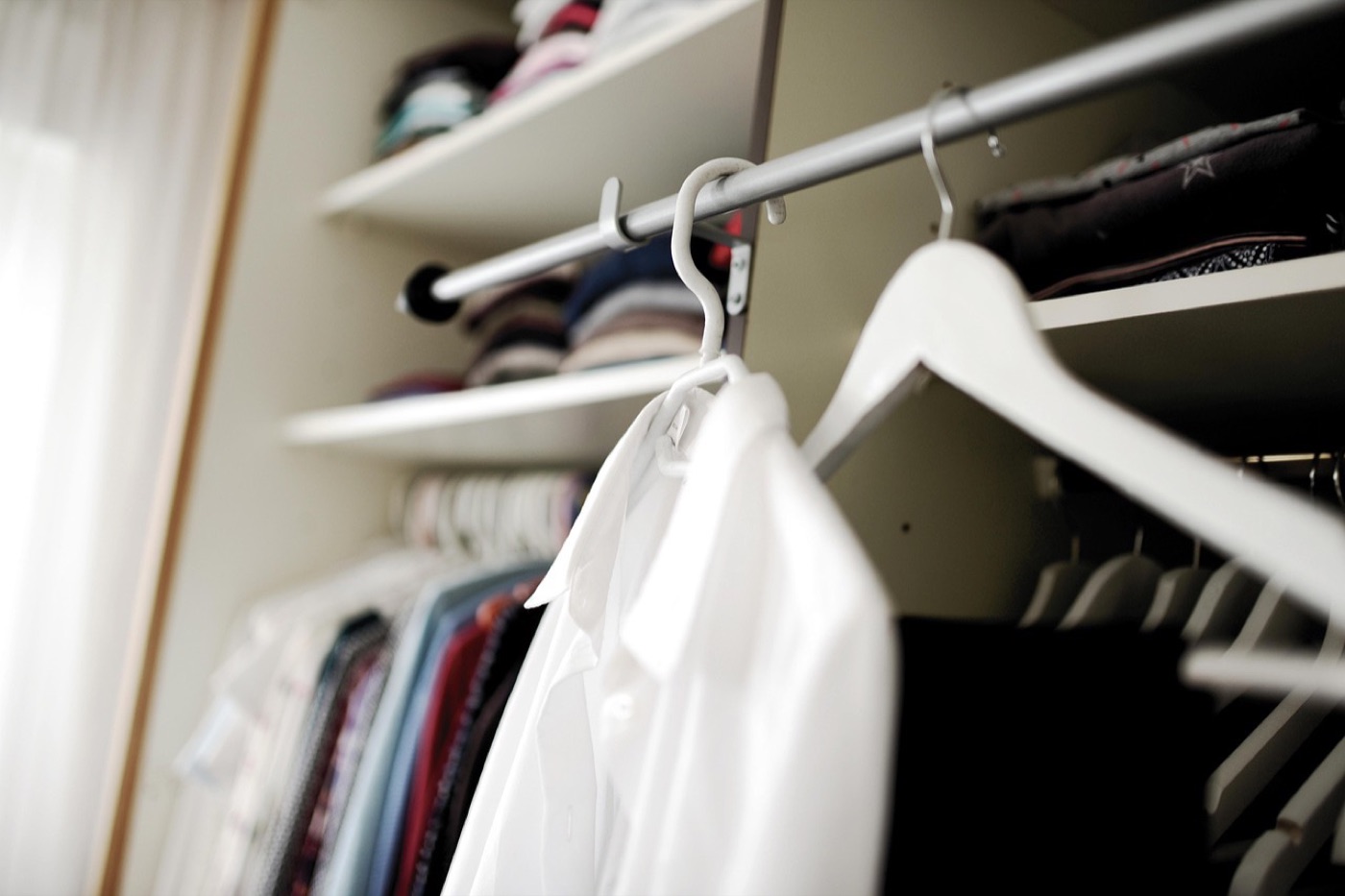 An open closet with folded stacks and a few hangers holding clothes