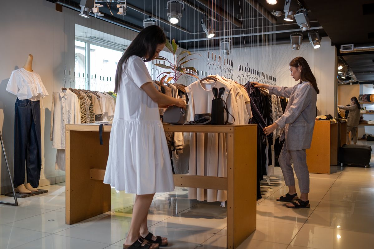Two shoppers browsing neutral-toned garments in a bright, independent clothing store